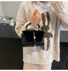 Detail of black suede and leather crossbody bag featuring gold buckle and handle