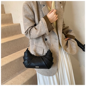 Detail of a black pleated crescent shoulder bag with a silver chain on a wool coat