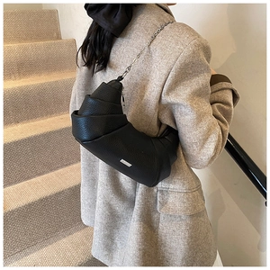 Detail of black pebbled leather croissant bag with silver chain strap on model shoulder