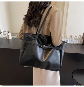Detail of a large black PU leather tote bag with buckle strap on a model shoulder