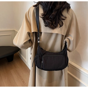 Dettaglio della borsa a tracolla nera in nylon minimalista con cinghia regolabile sul trench