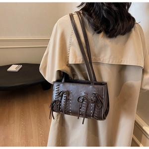 Detail of dark brown leather underarm bag with silver rivets and woven ties on model