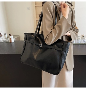 Detail of a black PU leather tote bag with silver buckle strap shown on a beige suit