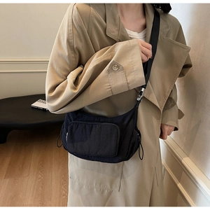 Dettaglio borsa a tracolla nera in nylon con coulisse laterale e tasche funzionali con zip