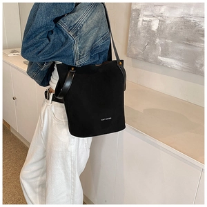 Détail du sac seau noir en daim mat avec clous dorés et bandoulière en cuir lisse