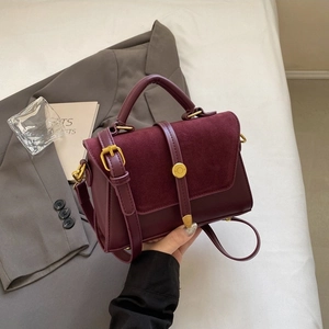 Chic burgundy faux leather and suede crossbody bag with gold hardware on a grey suit