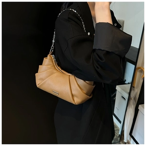 Detail of warm camel pleated cloud bag with silver chain strap on a black coat