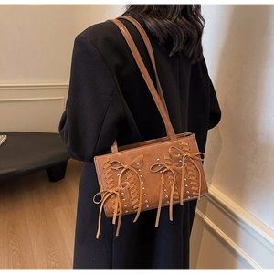 Detail of dark brown leather handbag with woven cut-outs, silver studs, and bow accents