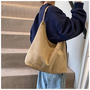 Gros plan du sac hobo en daim kaki porté par un mannequin dans un escalier minimaliste