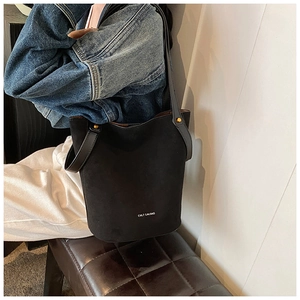 Détail d'un sac seau noir mat avec logo de marque et rivets dorés sur un modèle