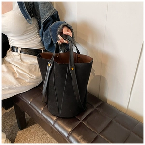 Détail d'un sac seau en cuir PU noir mat avec doublure marron et clous métalliques dorés