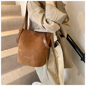 Sac seau en daim marron avec bordure en cuir lisse et rivets dorés porté à l'épaule
