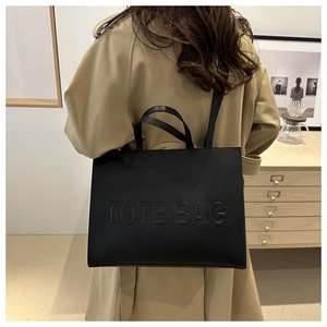 Detail of black faux leather tote bag with embossed text worn by a model in interior