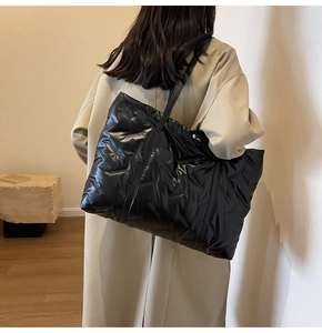 Détail d'un grand sac cabas noir en nylon matelassé porté avec un manteau beige