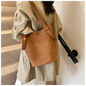 Détail d'un sac seau en PU marron mat porté avec un trench-coat classique kaki