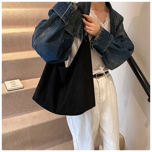 Détail d'un sac hobo noir minimaliste en tissu souple porté sur une veste en jean