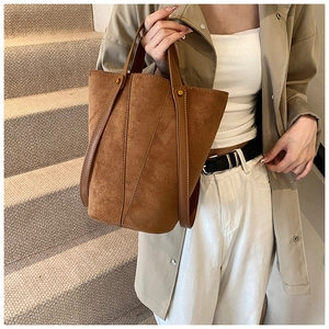 Détail d'un sac seau en daim marron avec des rivets dorés et des coutures élégantes
