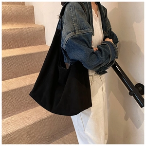 Détail d'un grand sac bandoulière en toile noire porté par un mannequin en extérieur