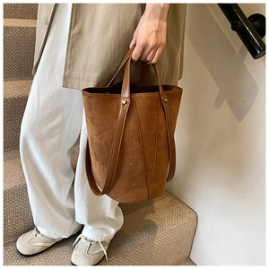 Détail d'un sac seau en daim marron avec rivets dorés et poignée en cuir lisse
