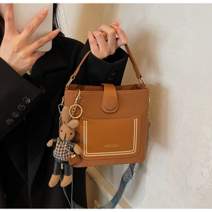 Detail of caramel PU leather bucket bag featuring a woven strap and plush rabbit charm