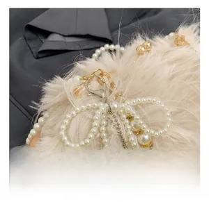 Close-up of golden lobster clasp and pearl chain on a beige plush shoulder bag