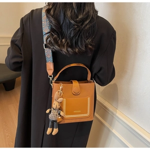 Detail of the caramel PU leather bucket bag with brand logo and woven shoulder strap