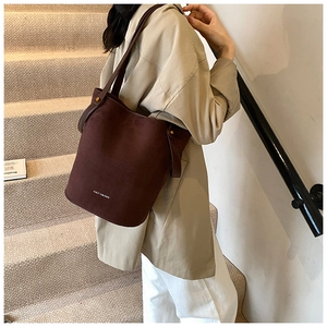 Détail d'un sac seau en daim marron foncé avec logo blanc et bandoulière large