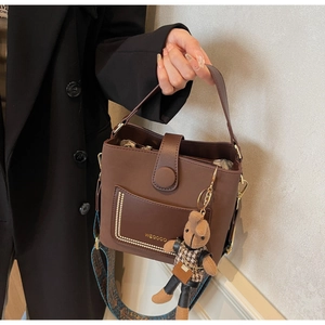 Detail of dark brown leather bucket bag with ethnic strap and small bear pendant charm
