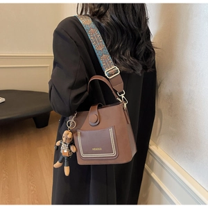 Close-up of brown PU leather crossbody bag with vintage patterned wide strap and bear charm
