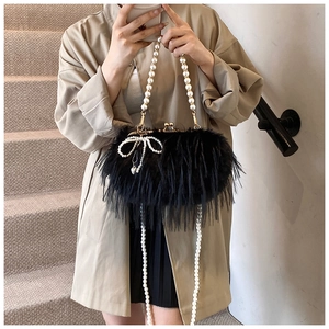 Detail of black plush crossbody bag featuring pearl bow and elegant pearl strap