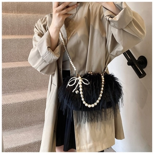 Detail of plush black shoulder bag with elegant pearl chains and a woven bow accent