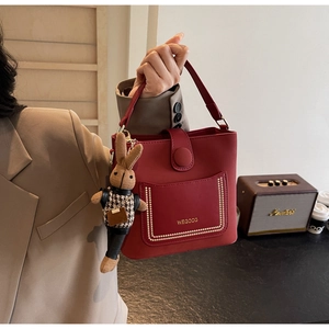 Detail view of red PU leather bucket bag featuring metal rivets and a cute rabbit pendant