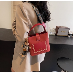 Detail of red PU leather bucket bag featuring a colorful jacquard strap and plush bunny charm