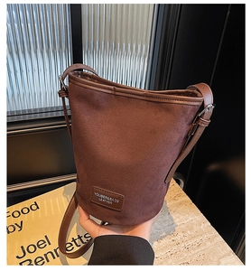 Detail of a brown bucket bag with mixed textures, leather label, and adjustable strap