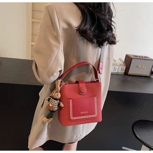 Close-up of a red PU leather bucket bag featuring gold studs and a woven guitar strap