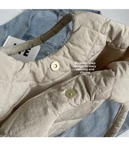 Detail showing the magnetic snap closure on a beige quilted puffer tote shoulder bag