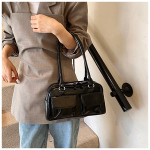 Detail view of a black patent leather shoulder bag with glossy finish and silver buckles