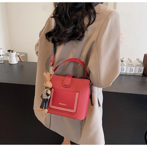 Red matte leather handbag with gold studs, wide patterned strap and a bunny charm