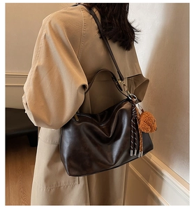 Detail of soft dark brown PU leather tote bag with teddy bear charm and tassel on a model