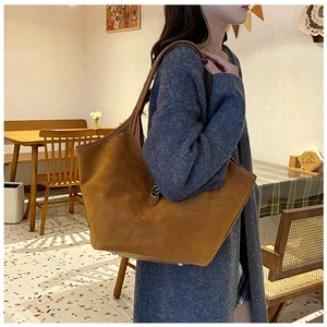 Close-up of brown suede tote bag featuring silver metal buckle and slender shoulder strap