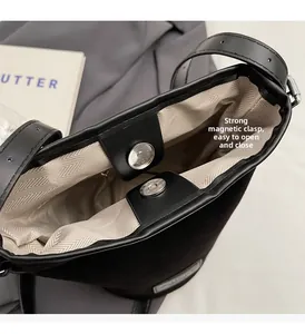 Detail of magnetic buckle closure and beige herringbone fabric lining on a black PU bag