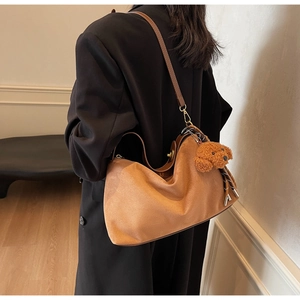 Detail view of brown faux suede hobo bag with teddy bear charm on black coat