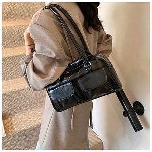 Detail of glossy black PU leather shoulder bag with two front flap pockets shown on model
