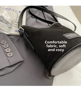 Detail of black frosted suede bucket bag with leather patch next to a gray suit jacket