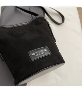 Close-up of black suede bucket bag with leather trim and shoulder strap detail
