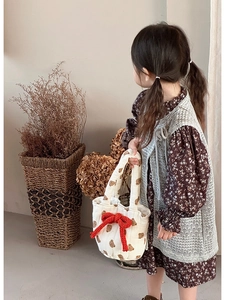 Detail view of children floral dress with a gray knit vest and a white bear quilted handbag