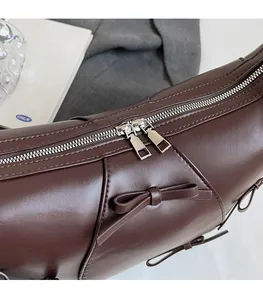 Gros plan des fermetures éclair argentées et du nœud en cuir sur le sac marron foncé