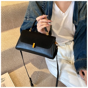 Close-up of matte black leather handbag with gold buckle and adjustable strap detail