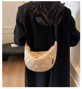 Detail of beige quilted crescent bag with black strap worn over a black autumn coat