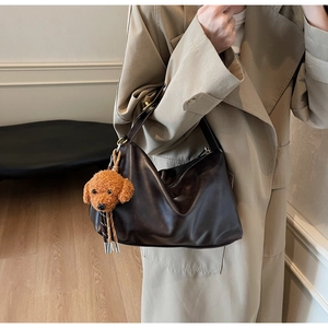 Detail of dark brown faux leather hobo bag featuring a cute poodle plush charm